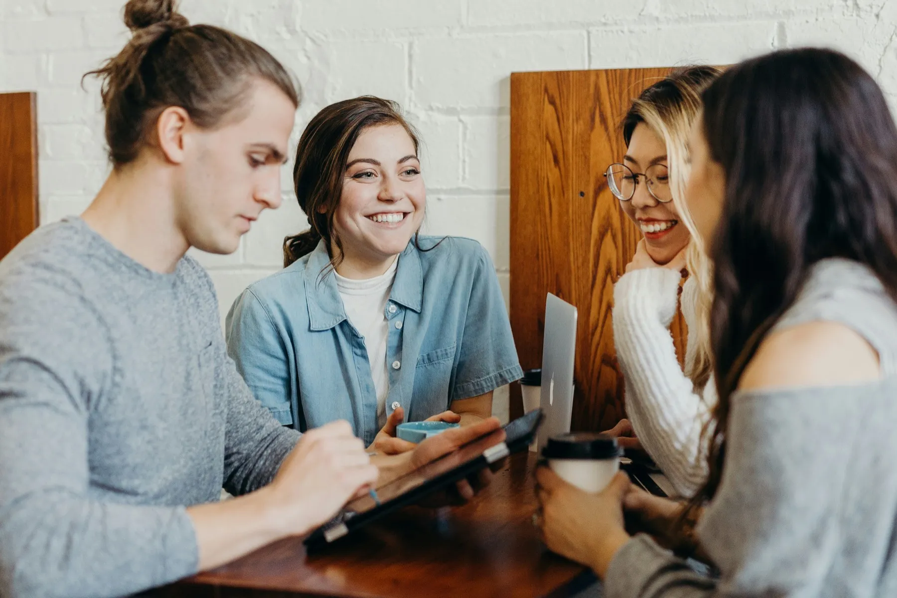 Four colleagues talking around a table with a laptop and coffee
